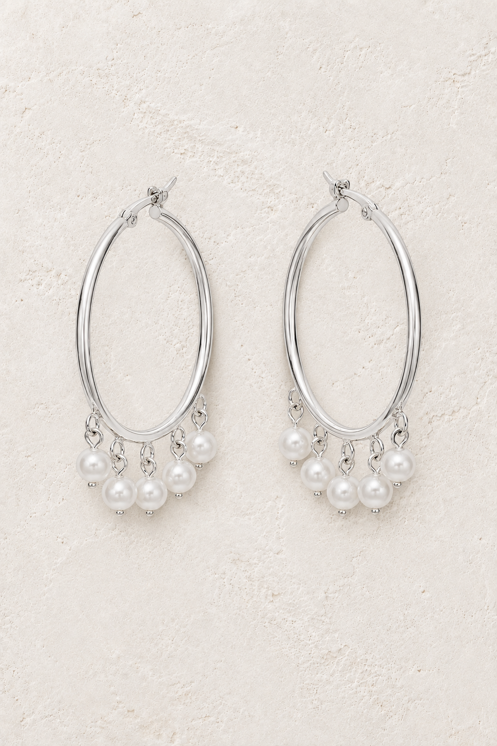 Sterling silver hoop earrings with pearl fringe on a warm off-white textured plaster background