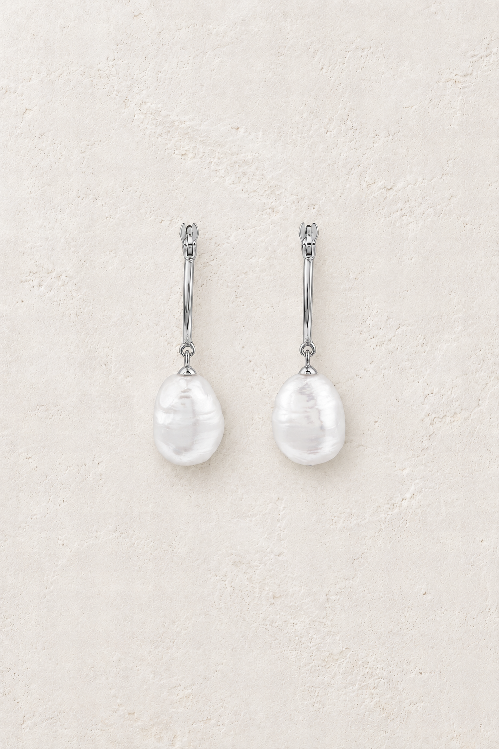 Sterling silver hoop drop earrings with single freshwater pearls on a warm off-white textured plaster background