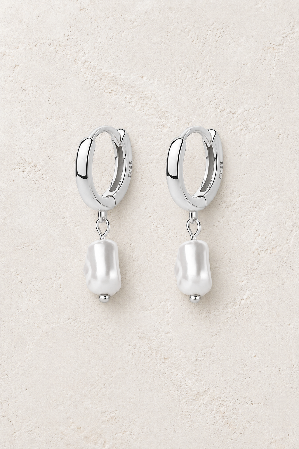 Sterling silver huggie earrings with square baroque pearl drops on a warm off-white textured plaster background