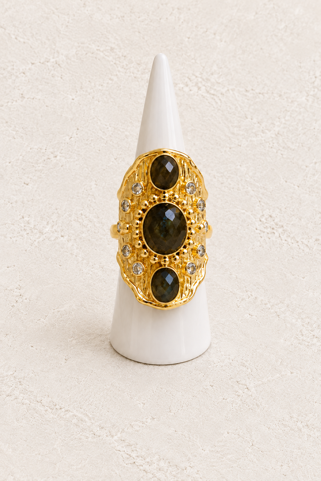 Solara Labradorite statement ring on white cone against warm textured background