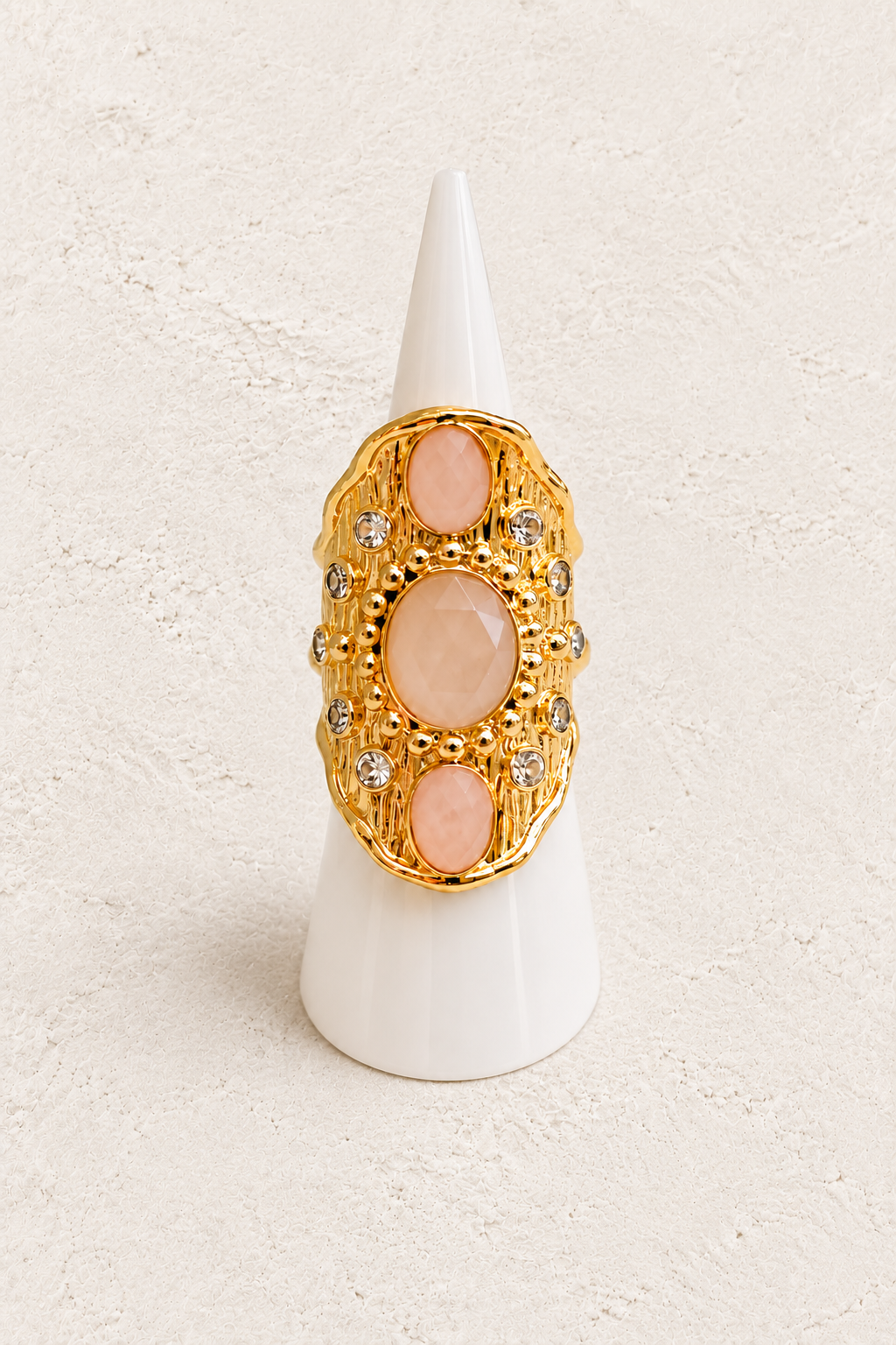 Solara Rose Quartz statement ring on white cone against warm textured background