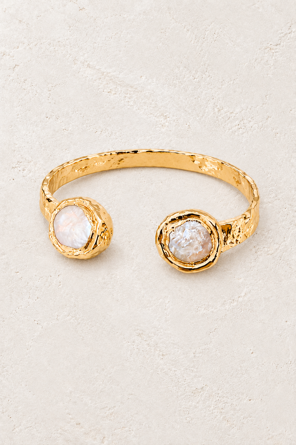 Thalassa gold cuff with circular freshwater pearls on a warm off-white textured plaster background