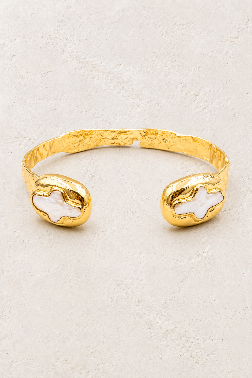 Thalassa gold cuff with pearly cross inlays on a warm off-white textured plaster background