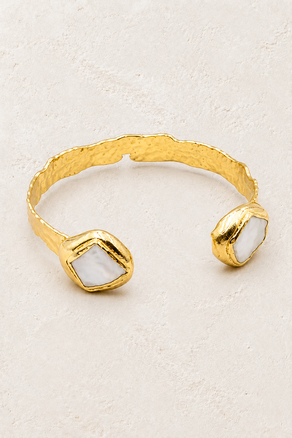 Thalassa gold cuff with oval and square freshwater pearls on a warm off-white textured plaster background