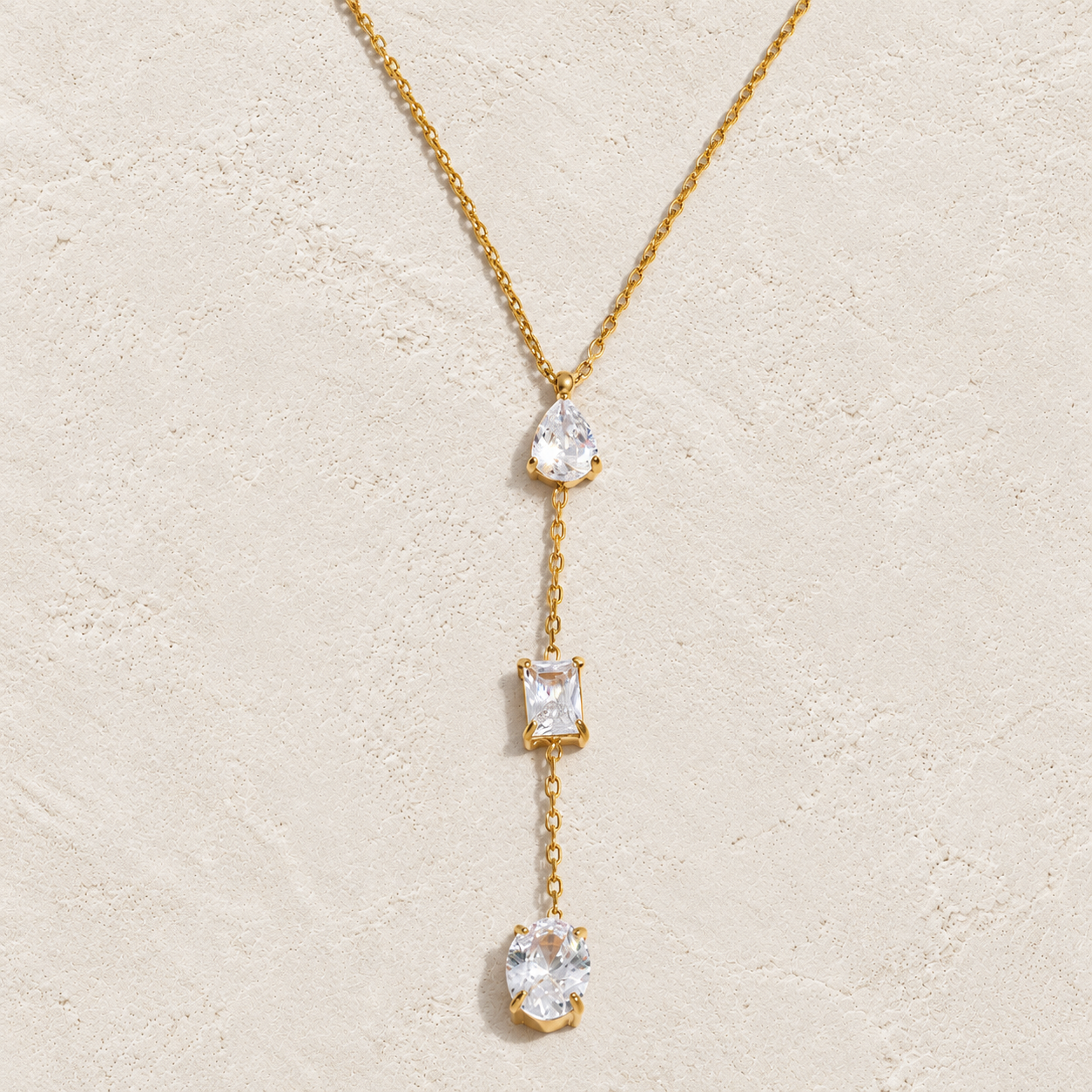 
                  
                    Gold three crystal lariat necklace on cream stone
                  
                