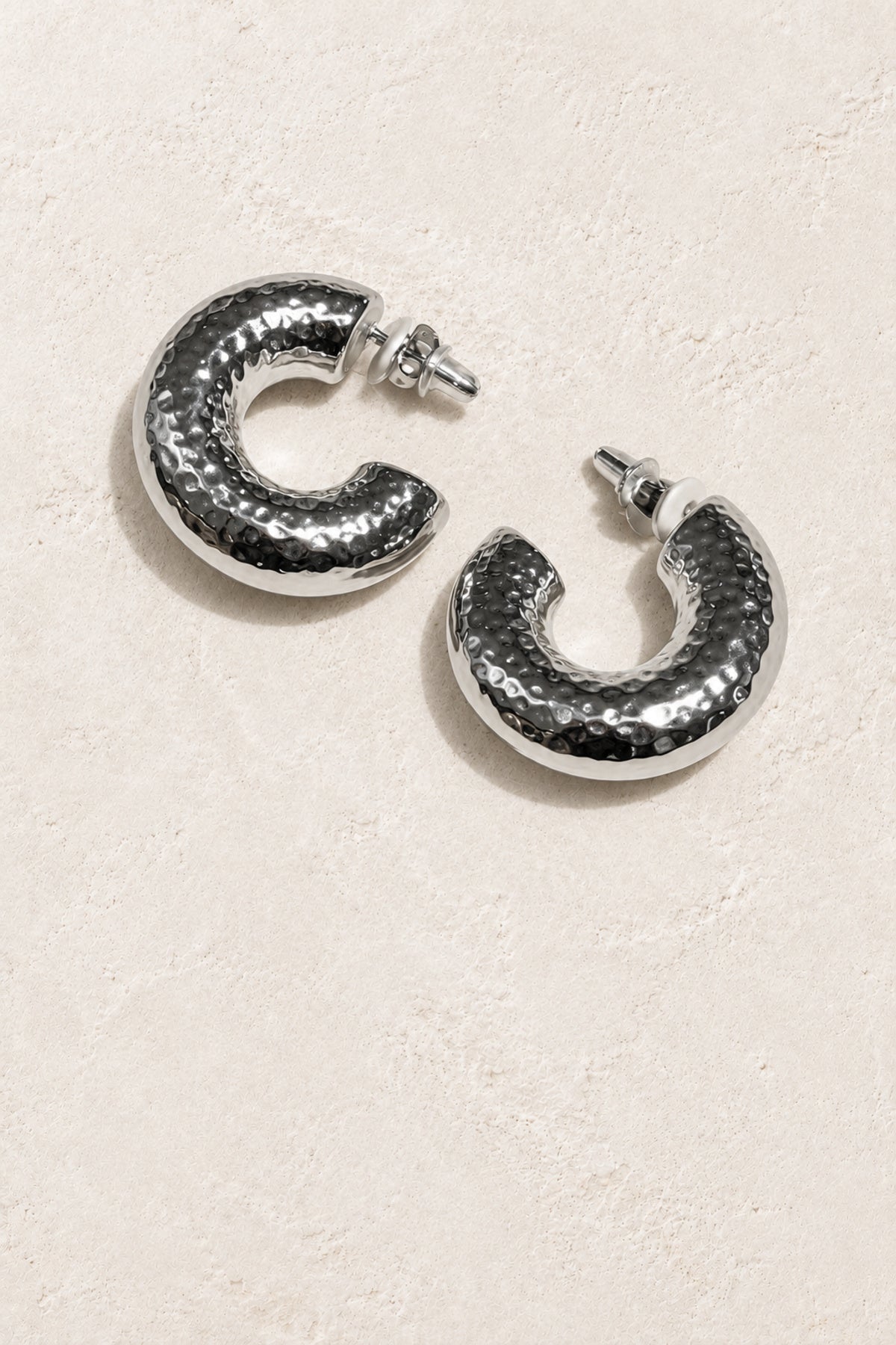 
                  
                    Zinnia Silver Hammered Hoop Earrings on warm ivory plaster
                  
                