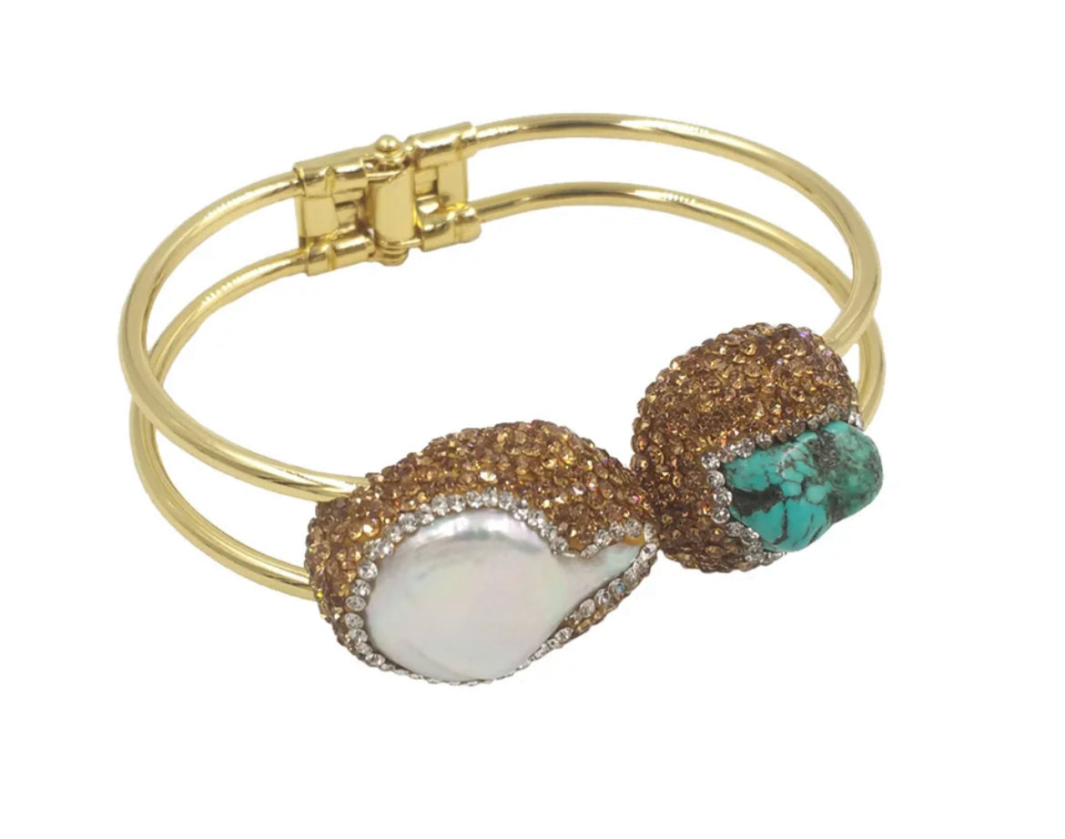 
                  
                    A gold-plated bangle bracelet with two decorative oval charms, one featuring a white mother-of-pearl inlay and the other featuring a turquoise stone surrounded by pavé crystals. 
                  
                
